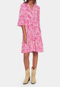 Rosa och krämfärgad mönstrad klänning med V-ringning, trekvartsärmar och utsvängd nederkant, kombinerad med beige cowboyboots.