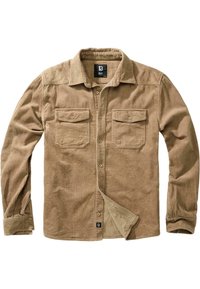 Chemise beige en velours côtelé à manches longues avec col, fermeture boutonnée devant, deux poches poitrine à rabat et poignets boutonnés, posée à plat sur fond blanc.