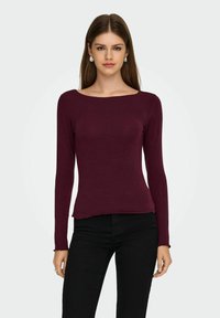 Bordeaux lange mouwen top met een brede halslijn, getailleerd ontwerp en licht gescheurde zoom. Gepaard met zwarte skinny jeans. Eenvoudige textuur.