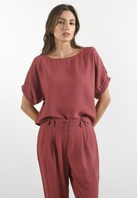 Volný top a ladící kalhoty z texturované tkaniny v burgundské barvě. Krátké rukávy a široký výstřih. Jemné švy v oblasti pasu.