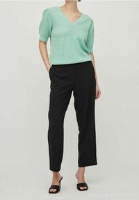 Maglietta tricot in verde menta con scollatura a V; pantaloni neri a gamba dritta; modella che indossa sandali neri con tacco. Design semplice e moderno.