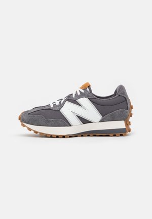 Baskets lacées grises et blanches avec des panneaux en suède et mesh, semelle en gomme et grand logo blanc "N" sur le côté, présentées sur un fond uni.