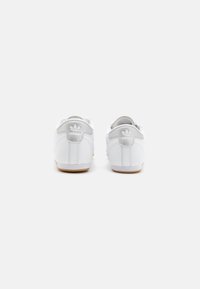White sneakers with a smooth leather upper, gray accents on the heel, and a brown rubber sole. Features classic adidas logo on the back.