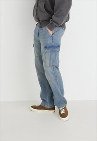 Lys blå cargo-bukser med flere lommer, laget av denim. Har en avslappet passform og kontrastsøm. Matchet med brune joggesko.
