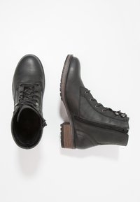 Botas de cuero negro hasta el tobillo con cordones en la parte delantera, cremallera lateral y suela de goma texturizada con tacón de madera. Los detalles incluyen ojales metálicos.