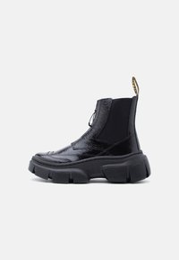 Γυαλιστερό μαύρο χοντρό μποτάκι πλατφόρμας στον αστράγαλο με ελαστικό πλαϊνό πάνελ και θηλιά έλξης σε λευκό φόντο.