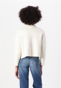 Pull en ivoire coupé avec un motif côtelé texturé, col haut et coupe loose. Assorti à un jean en denim bleu taille haute.
