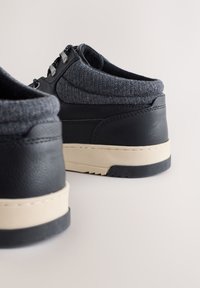 Čierne kožené topánky so sivými filcovými akcentmi, zaobleným tvarom, krémovými gumovými podrážkami, kovovými očkami a švami na vrchnej časti.