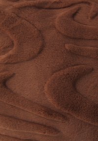 Tessuto in peluche marrone con un motivo ondulato e testurizzato. La superficie è morbida con una finitura liscia e una profondità variabile nel design.