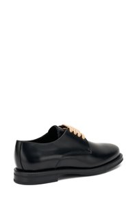 Zwarte leren schoen met een ronde neus, textuur, voorzien van beige veters en een platte zwarte rubberen zool, die een eenvoudig, klassiek ontwerp benadrukt.