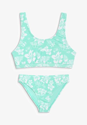 Maillot de bain deux pièces vert menthe avec motifs de fleurs et feuilles d’hibiscus blancs, comprenant un haut style brassière sportive et un bas de bikini assorti.