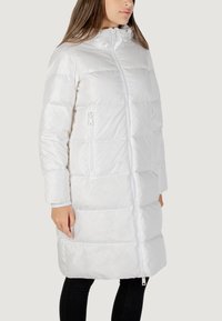 Cappotto puffer bianco con colletto alto, zip a tutta lunghezza e tasche laterali con zip. Presenta un design trapuntato e polsini elasticizzati.