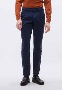 Mörkblå chinos med en slät textur, med rak skärning, två framfickor och knappstängning framtill. Bärs med svarta loafers.