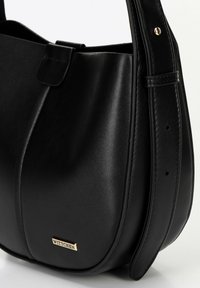Black leather handbag with a smooth texture, curved body design, and a short strap. Features a gold-tone logo and subtle stitching accents.