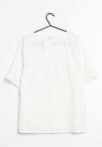 Chemise blanche à manches courtes élastiques ; texturée avec des motifs de diamants brodés ; tombe jusqu'à la taille ; suspendue à un crochet noir.