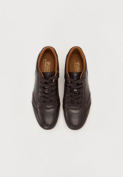 Baskets en cuir marron avec un design perforé, intérieur contrastant en beige, bout rond et fermeture à lacets. Logo de la marque visible sur le côté.