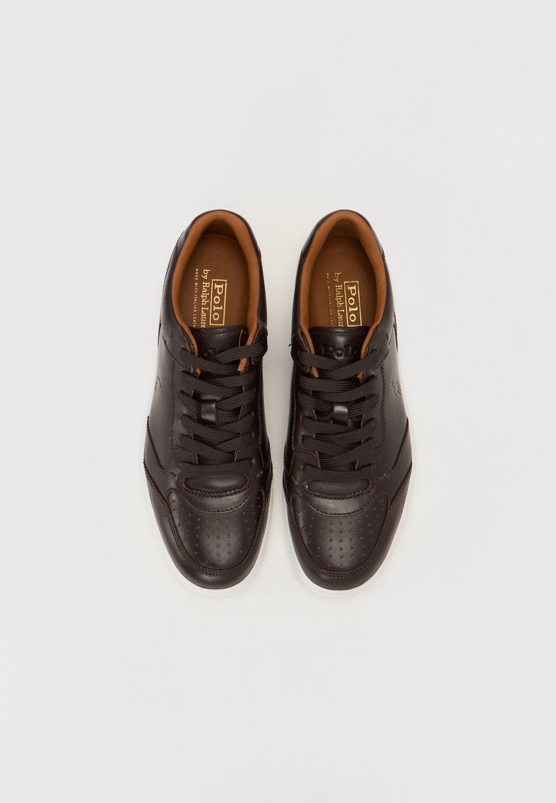 Baskets en cuir marron avec un design perforé, intérieur contrastant en beige, bout rond et fermeture à lacets. Logo de la marque visible sur le côté.