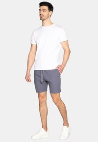 Shorts grigi con cintura elastica e cordoncino, abbinati a una t-shirt bianca semplice. Indossati con delle sneakers bianche. Design semplice, vestibilità casual.