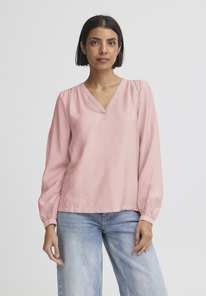 Světlounce růžová blůza s dlouhým rukávem a výstřihem do V, s nařasenými rukávy a hladkou strukturou, kombinovaná se světle modrými džínami.