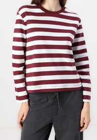 Maglione a righe bordeaux e bianco a maniche lunghe in cotone morbido, con colletto a girocollo e vestibilità rilassata, abbinato a pantaloni grigi scuri con coulisse.