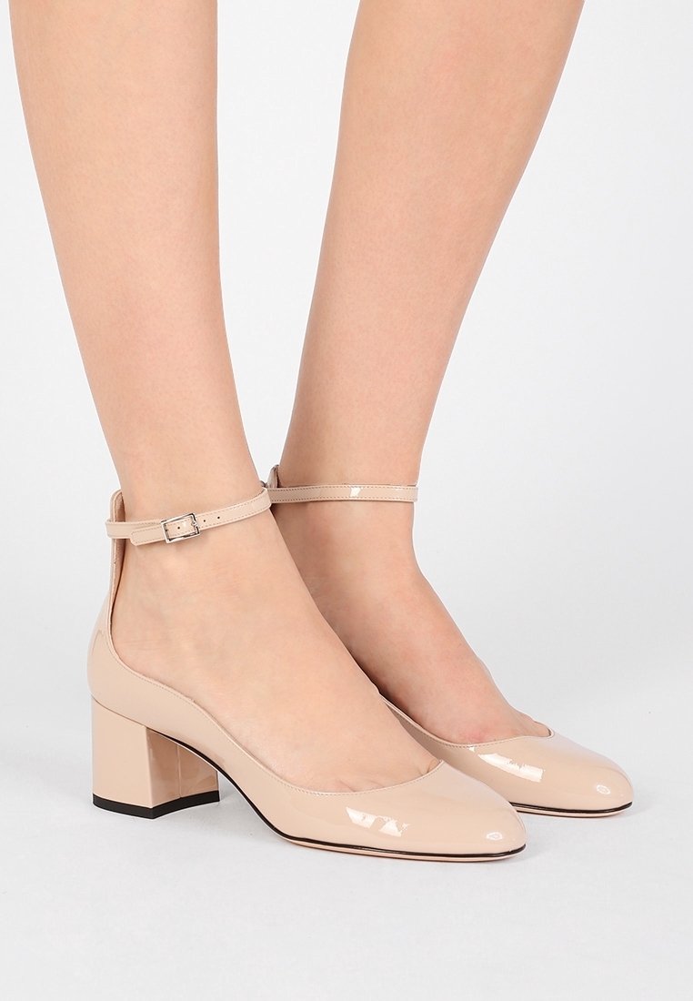 Scarpe con tacco in pelle verniciata beige, con tacco quadrato, punta arrotondata e cinturino alla caviglia con dettaglio in fibbia argentata.