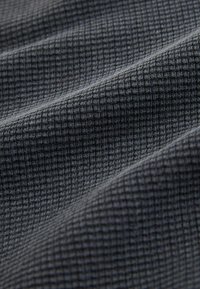 Teksturowana tkanina w ciemnoszarym kolorze, z wzorem w kratę z wypukłymi kwadratami, prezentująca miękki, tkany wygląd i delikatny połysk.