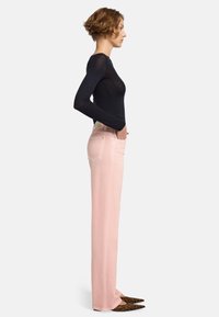 Jeans dritti rosa chiaro con tasche laterali e cuciture minime. Abbinati a un top nero aderente a maniche lunghe e scarpe con stampa leopardata.