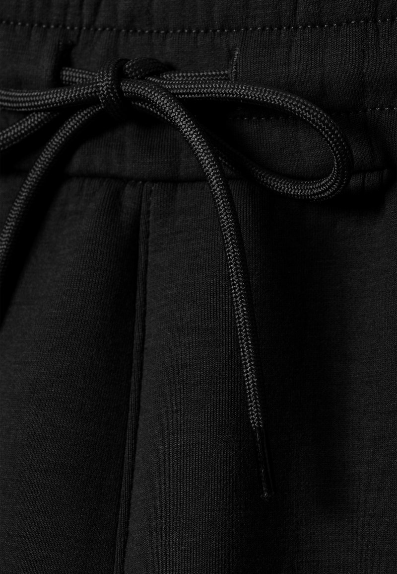 Cordon de serrage noir à la taille en tissu doux et texturé avec un cordon tissé. À l'avant, il présente des détails cousus et un pli pour une coupe décontractée.