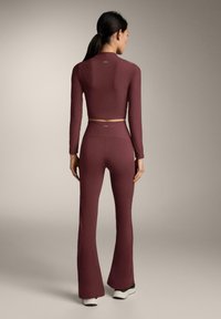 Donkerrode geribbelde tweedelige outfit met lange mouwen en uitlopende broek. Gladde textuur, aansluitend ontwerp, en minimale branding aan de achterkant.