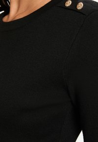 Maglione nero a maglia con scollo a girocollo, tessuto texturizzato e due bottoni decorativi dorati sulla spalla.