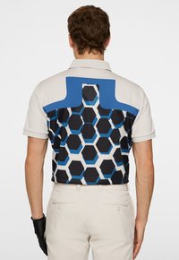 Kortärmad polotröja med en ljusgrå framsida och en baksida med ett svart och blått hexagonmönster, accentuerad med en solid blå krage.