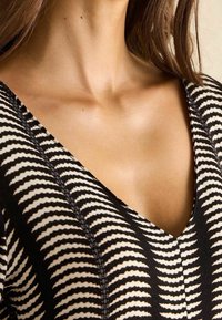 La tela a rayas negra y crema presenta un diseño de cuello en V y un patrón texturizado, destacando una silueta ajustada y colores contrastantes.