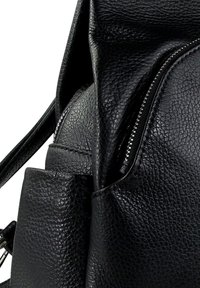 Gros plan sur un sac à dos en cuir noir texturé avec une fermeture éclair visible et une poche latérale.