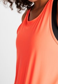 Camiseta sin mangas deportiva hecha de una suave tela naranja brillante, con cuello redondo y un diseño ajustado que permite libertad de movimiento.
