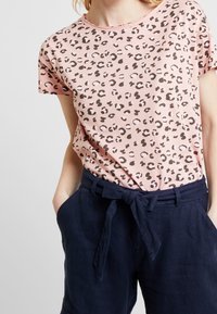 Camiseta de manga corta rosa con un estampado de leopardo, combinada con pantalones de lino azul marino que presentan un detalle de cintura atada.