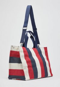 Sac fourre-tout en toile avec des rayures horizontales rouges, bleu marine et blanches. Orné d'une bandoulière bleue amovible et de deux poignées.
