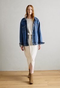 Veste en jean bleue, oversize avec poches à rabat. Pull côtelé gris clair en dessous. Jupe crème avec une fente sur le devant. Bottines à talons en imprimé léopard.