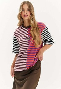 Pasiasta koszulka z krótkim rękawem z różnorodnymi kolorami, w tym brązowym, różowym, czerwonym i czarnym. Haftowany detal motyla na klatce piersiowej.