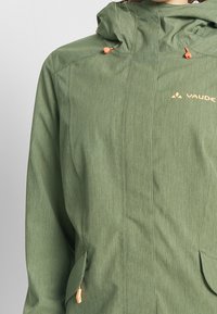 Green lightweight jacket with a textured finish, featuring orange drawstrings, a hood, and two front pockets. Brand name visible on chest.