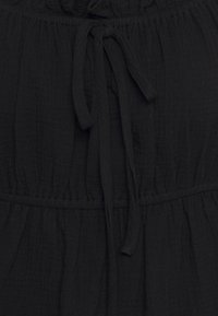 Abito di cotone nero con tessuto texturizzato, caratterizzato da vita cinchata e un nodo anteriore. Il design presenta un colletto arr gathered e una vestibilità morbida.