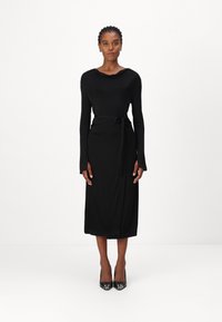 Svart tettsittende kjole med lange ermer, drapert halslinning og knyttet belte som fremhever livet. Glatt stoff, ankel-lengde, minimalistisk design.