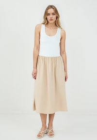 Débardeur blanc à encolure dégagée associé à une jupe beige longueur genou. Tissu lisse avec une taille élastique et une texture douce.