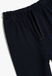 Pantalones de canalé azul marino con cintura elástica, cordón ajustable y bolsillos laterales. Textura suave con un diseño ajustado.