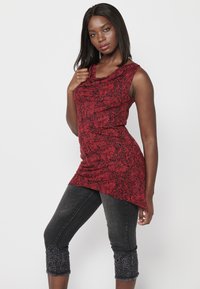 Haut sans manches rouge avec un motif floral et un design asymétrique. Associé à un jean foncé orné de broderies détaillées à l'ourlet court.