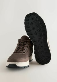 Braune Leder Schnürstiefel mit dicker, cremefarbener Sohle und schwarzer rutschfester Außensohle, die ein Grip-Muster und den Markennamen "NEXT" zeigt.