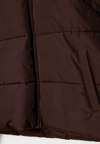 Brązowa kurtka puchowa z zapięciem na zamek, poziomym przeszyciem i boczną kieszenią, wykonana z gładkiego, lekkiego materiału.