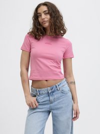 Tettsittende, kortermet, rosa crop-top med teksten "A LITTLE BIT DRAMATIC". Kombinert med lyseblå, avslappede jeans. Glatt tekstur.