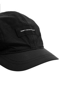 Gorra negra con diseño estructurado, hecha de tela ripstop, con una etiqueta prominente en la parte delantera y un visera curvada.