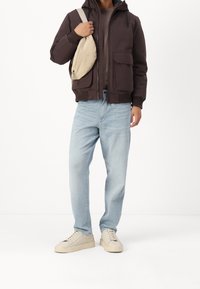 Brązowa kurtka z kapturem z przednimi kieszeniami, pod spodem szara koszula, jasnoniebieskie dżinsy i beżowe trampki; mała kremowa torebka na ramię.