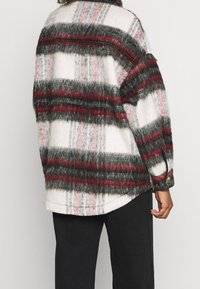 Överdimensionerad rutig skjorta med en fluffig textur, prydd med svarta, röda och vita ränder. Knappar på ärmsluten och rundad nederkant.